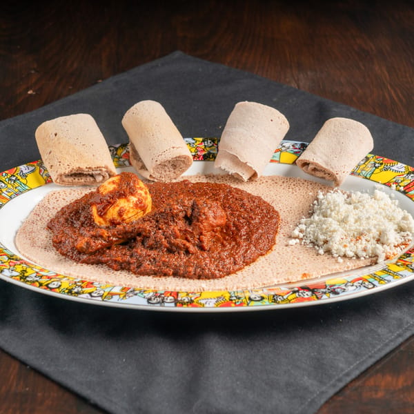 Ethiopian Doro Wat, a spicy chicken stew with a hard-boiled egg, injera, and crumbled cheese.