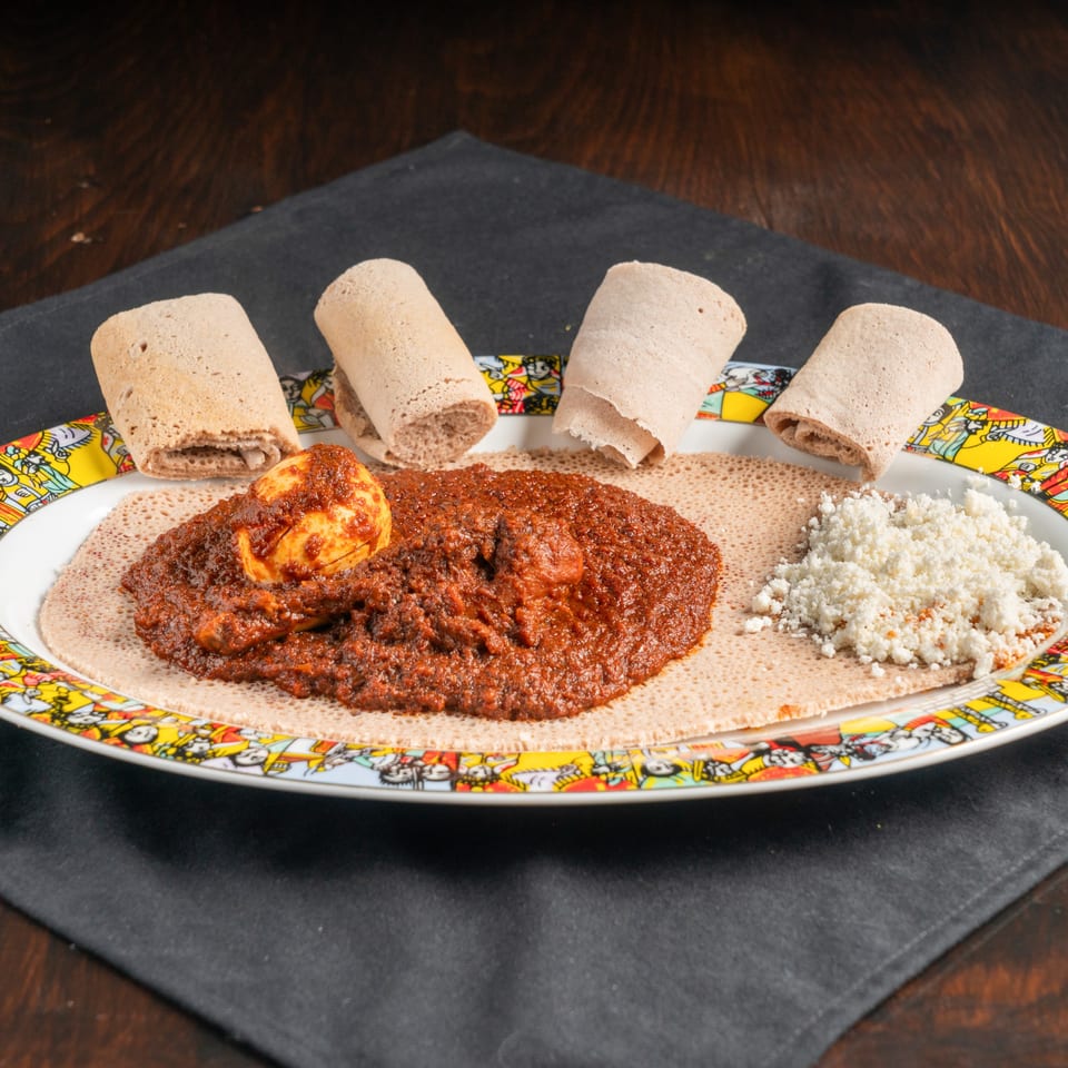 Ethiopian Doro Wat, a spicy chicken stew with a hard-boiled egg, injera, and crumbled cheese.
