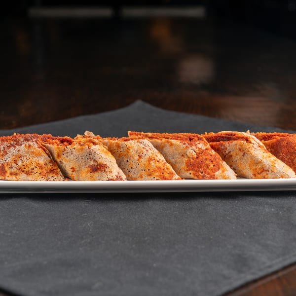 Close-up of several injera rolls, sprinkled with red spice, on a white rectangular plate.