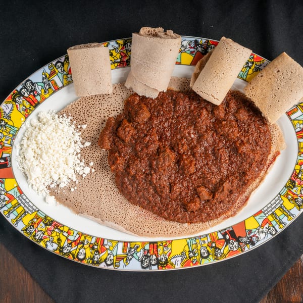 Ethiopian injera bread with a rich, dark red stew and a side of white crumbled cheese.