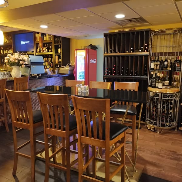 A bar area with tall wooden chairs, a black table, and shelves of wine bottles.