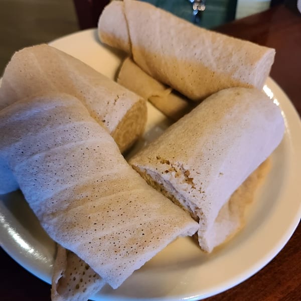 Several rolls of light, spongy injera bread, a staple of Ethiopian cuisine, on a white plate.
