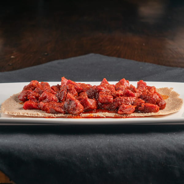 Spicy red Ethiopian tibs, a meat dish, served on injera bread on a white rectangular plate.