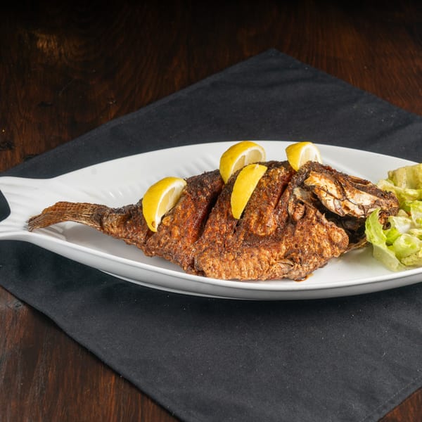 Whole fried fish garnished with lemon wedges and a side of lettuce on a white fish-shaped plate.
