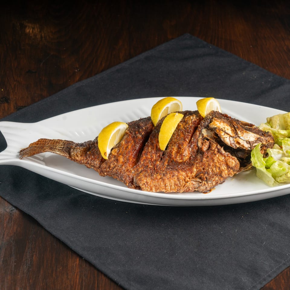 Whole fried fish garnished with lemon wedges and a side of lettuce on a white fish-shaped plate.