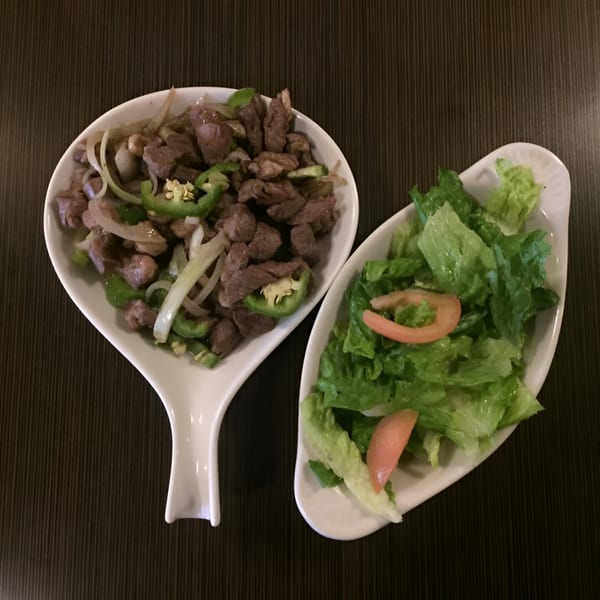 Ethiopian beef tibs with onions and peppers, alongside a fresh green salad with tomato slices.